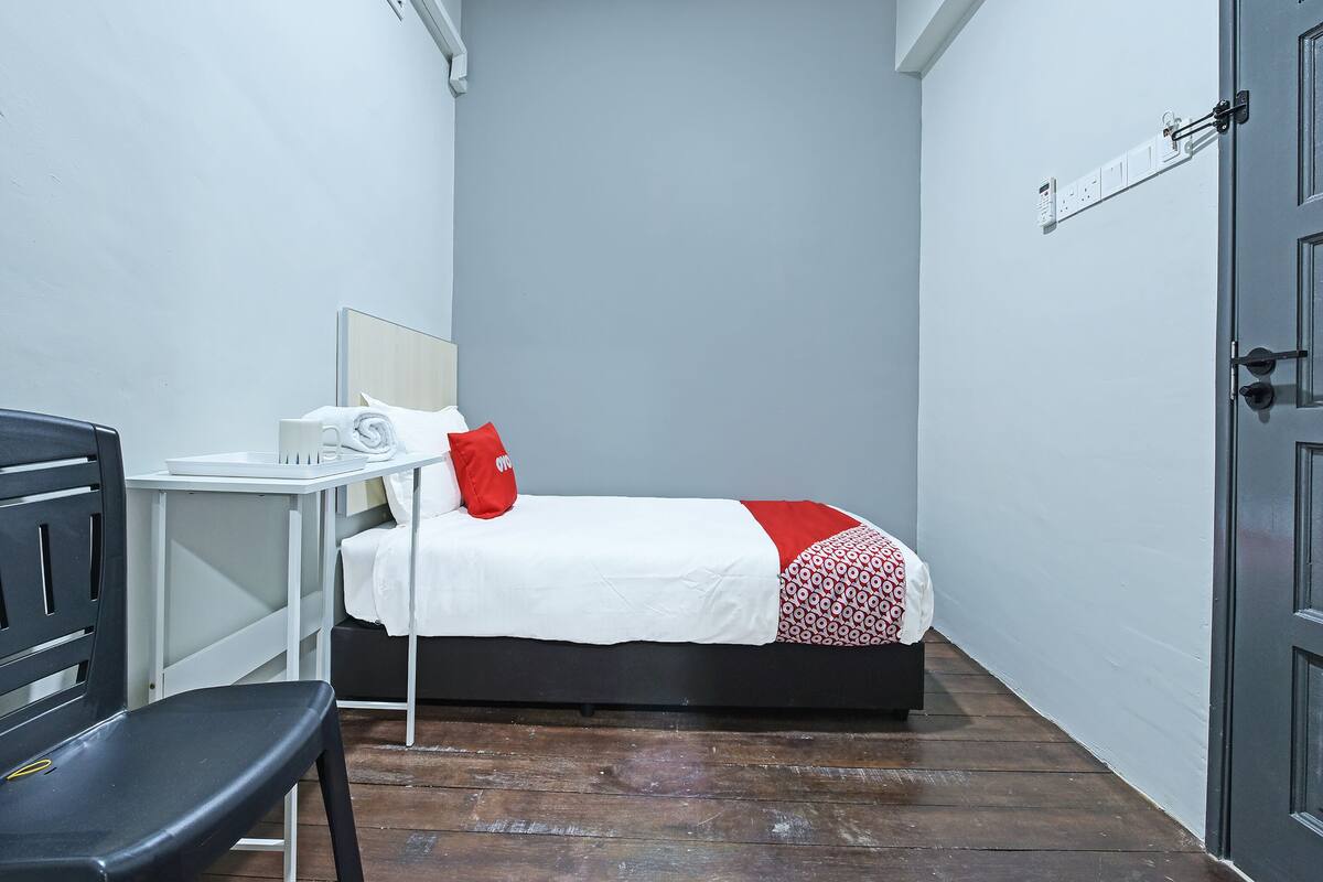 Habitació petita i ordenada amb un llit, una cadira, una taula i una porta.