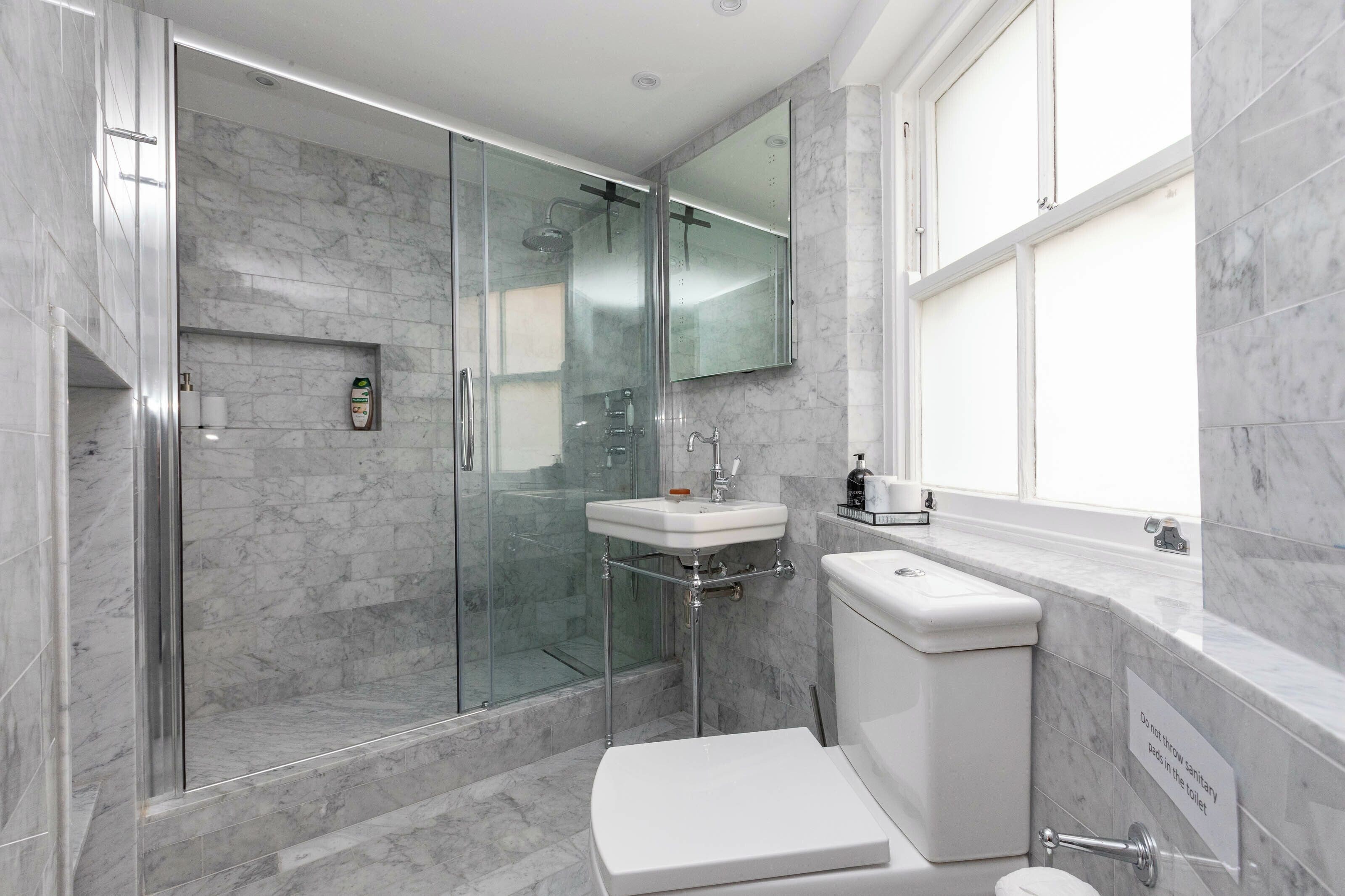 Un baño moderno con ducha envuelta en cristal, un lavamanos blanco y un inodoro.