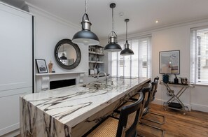 A kitchen with a marble countertop, pendant lights, a built-in oven, and a window with blinds.