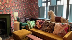 Ein gemütliches Wohnzimmer mit strukturiertem Wandpapier, einem grünen Sofa, einem gelben Sessel und einem Kamin.