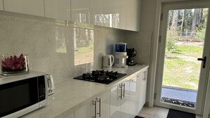 A modern kitchen with white cabinets, a microwave, a gas stove, and a coffee maker. - Cosy apartment close to Puffing Billy  (Clematis)