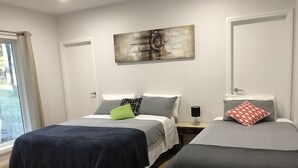 A hotel room with two beds, a large abstract painting on the wall, a window with curtains, and a door. - Cosy apartment close to Puffing Billy  (Clematis)