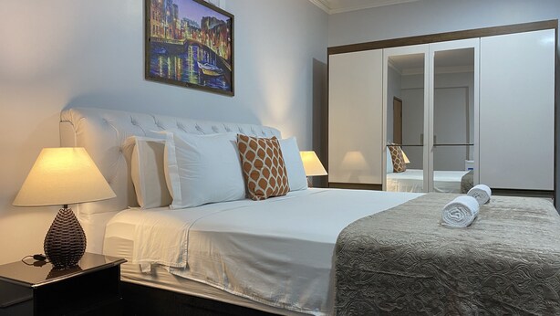 Ein Hotelzimmer mit einem großen Bett, zwei Nachttischlampen, einem Stadtbild und einem Kleiderschrank sowie einem Spiegel.