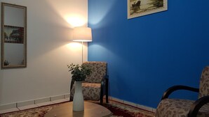 Ein Zimmer mit blauer Akzentwand, einem runden Tisch mit einer Vase, einem Stuhl und einer Lampe.
