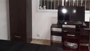 A bedroom with a bed, a TV on a stand, a wardrobe, and a window with bars.