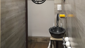 A bathroom with a shower, a sink with a black basin, and a wall-mounted toilet.