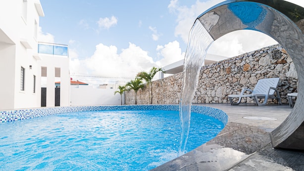 Ein Swimmingpool mit klarem, blauem Wasser, einer Steinmauer und einem weißen Gebäude im Hintergrund.