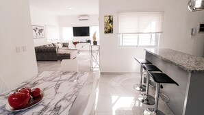 Eine moderne Küche mit Marmorarbeitsplatte, einer Bar mit Hockern und einem Wohnzimmer mit Sofa und Flachbildfernseher.