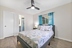 Ein Schlafzimmer mit einem Bett, einem Deckenventilator, einem Fenster mit blauen Vorhängen und einer Tür.