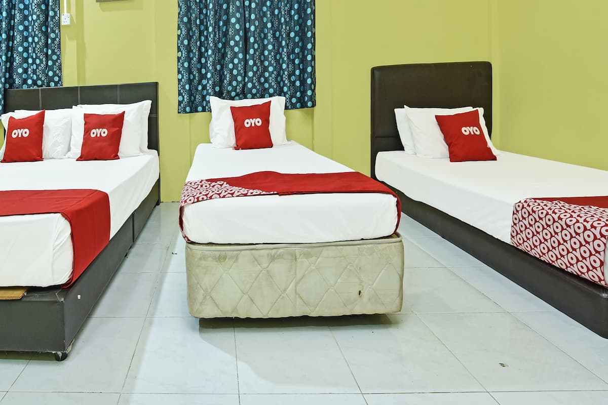 Habitación de hotel con tres camas individuales, cada una con cubrecama y almohadas rojo y blanco. El piso es de baldosas y la pared es de color amarillo liso.