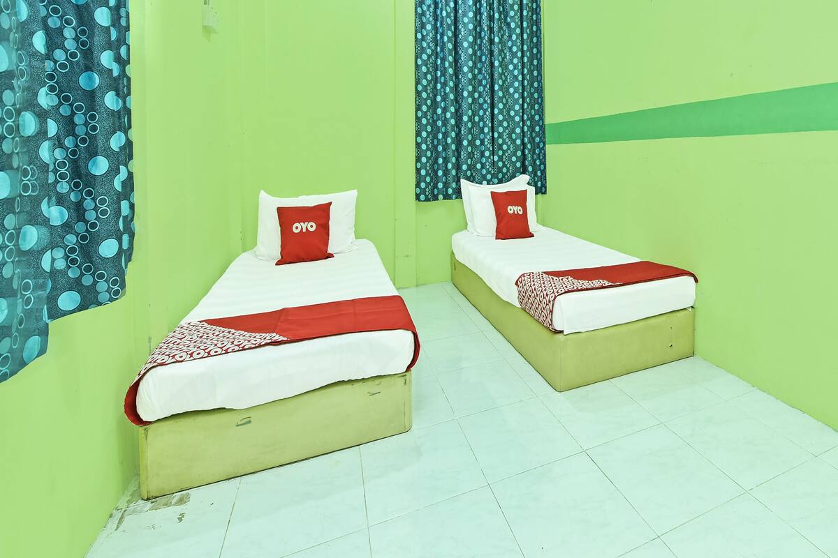 Dos camas individuales con ropa de cama roja y blanca, una pared verde y cortinas estampadas.