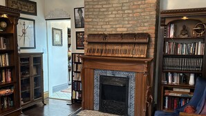 Ein gemütliches Wohnzimmer mit Kamin, Bücherregalen, einem blauen Sofa und einem gemusterten Teppich.