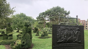 Ein gepflegter Garten mit geschnittenen Formschnitten und einem historischen Pfeiler.