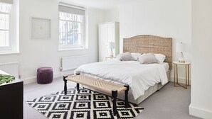 Une chambre à coucher avec un lit, des tables de chevet, un banc, un tapis à motifs et une fenêtre.