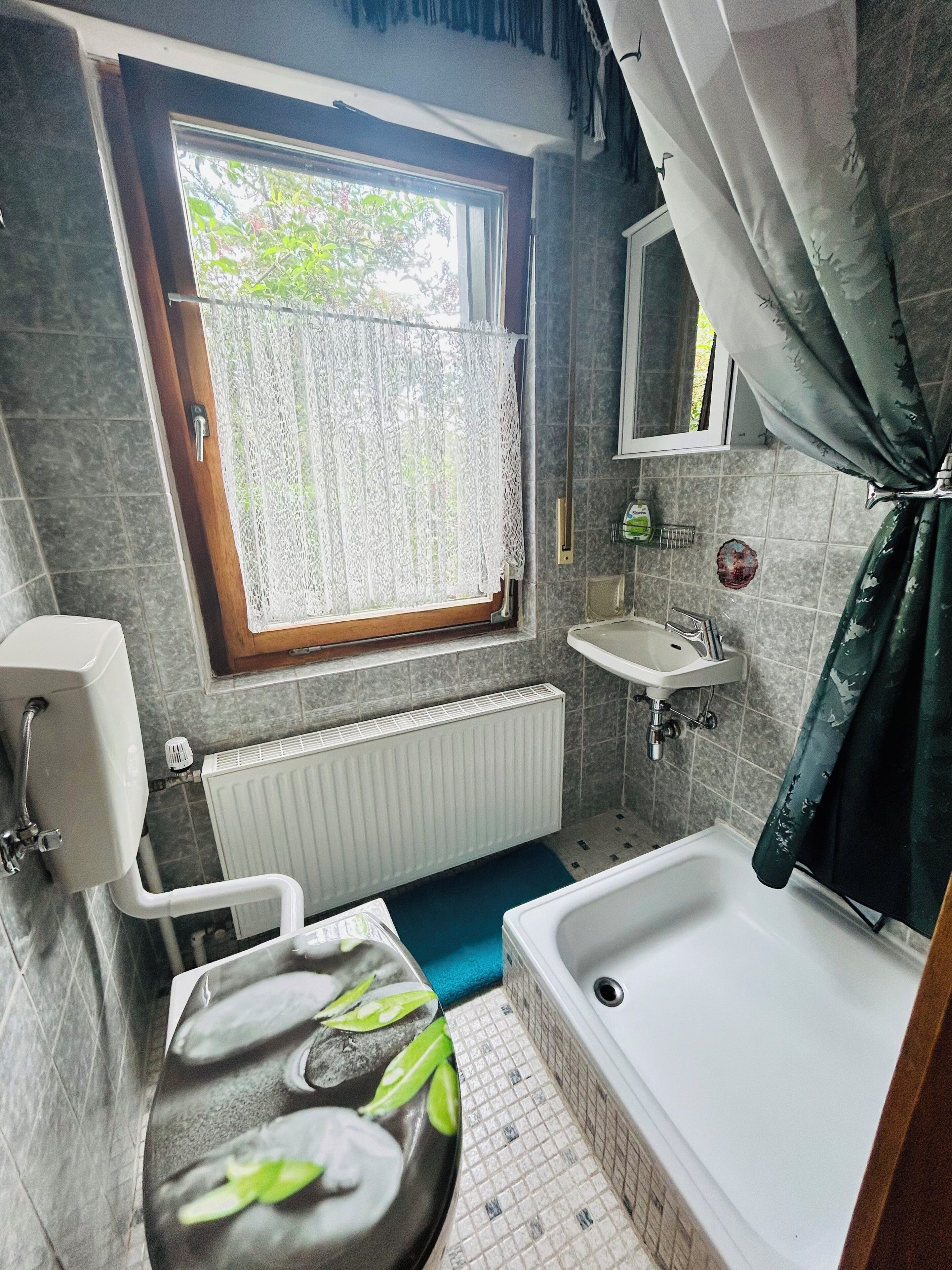 A bathroom with a bathtub, a toilet, a sink, and a window with a lace curtain.