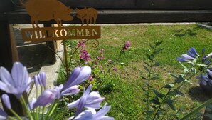 Un panneau en bois représentant un cochon et le mot « WILKOMMEN », indiquant une zone d’accueil, entouré de verdure et de fleurs.