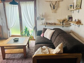 Un salon chaleureux avec un canapé marron, une table basse en bois et une grande fenêtre ornée de rideaux légers.