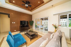 A spacious living room with a ceiling fan, a flat-screen TV, a sofa, a blue armchair, and a coffee table.