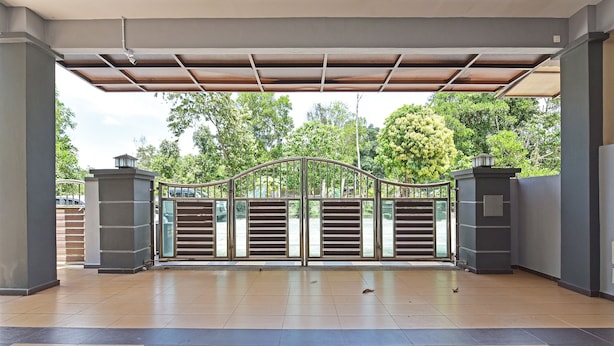 A covered entrance with a metal gate, tiled floor, and a view of trees and parked cars. - OYO Home 90582 Dz Homestay Bukit Ubi (Kuantan)