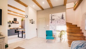 Un'ampia zona giorno con una scala in legno, una poltrona blu e una cucina sullo sfondo.