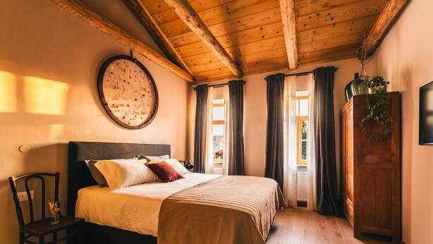 Una camera da letto con un letto in legno, una sedia, un orologio da parete rotondo e un armadio in legno.