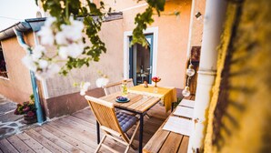 Un'area esterna con decking in legno, un tavolo, sedie, una porta e una pianta in vaso.