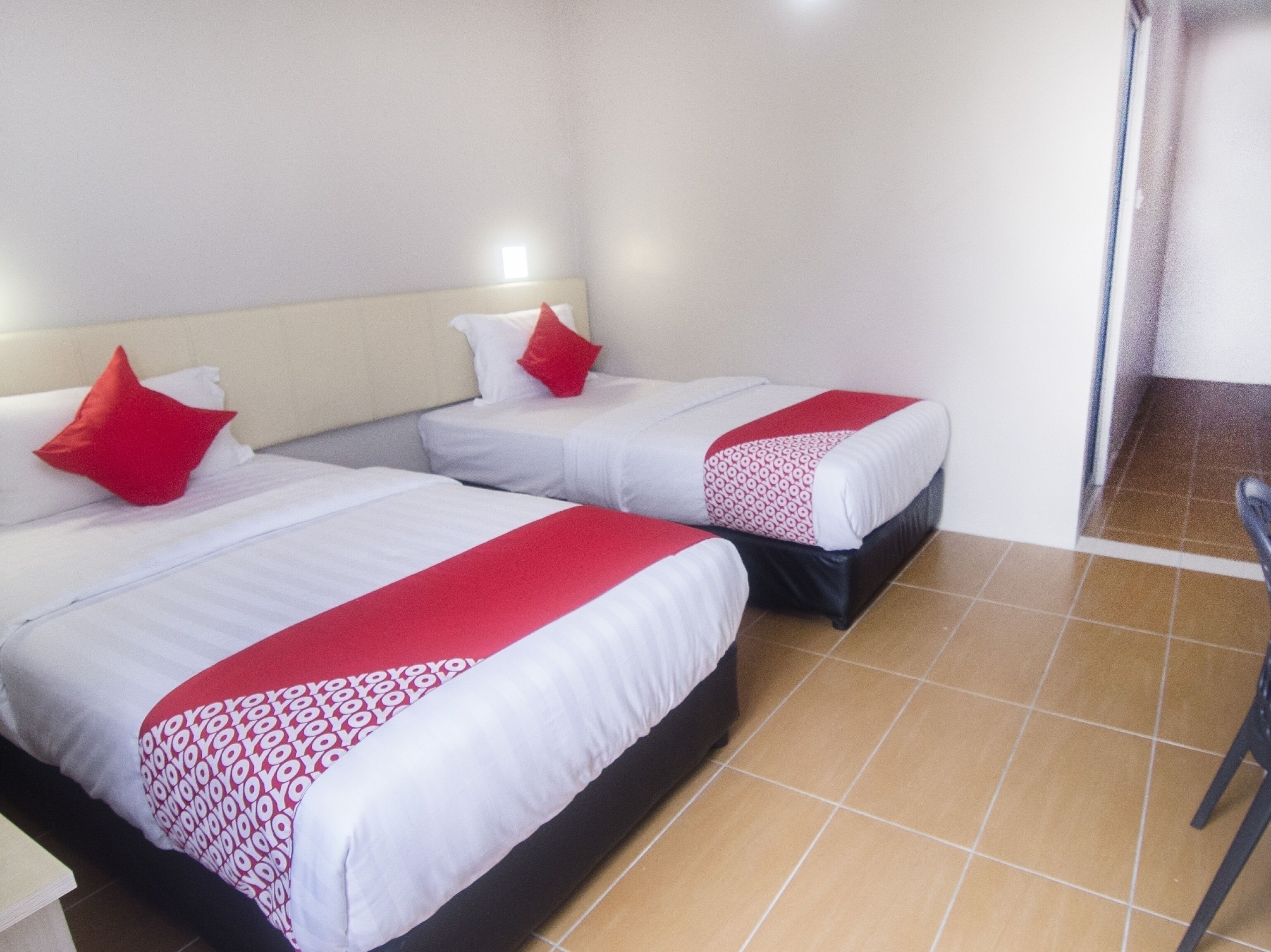 Habitación de hotel con dos camas, cada una con ropa de cama blanca y detalles en rojo, y suelo de baldosas.