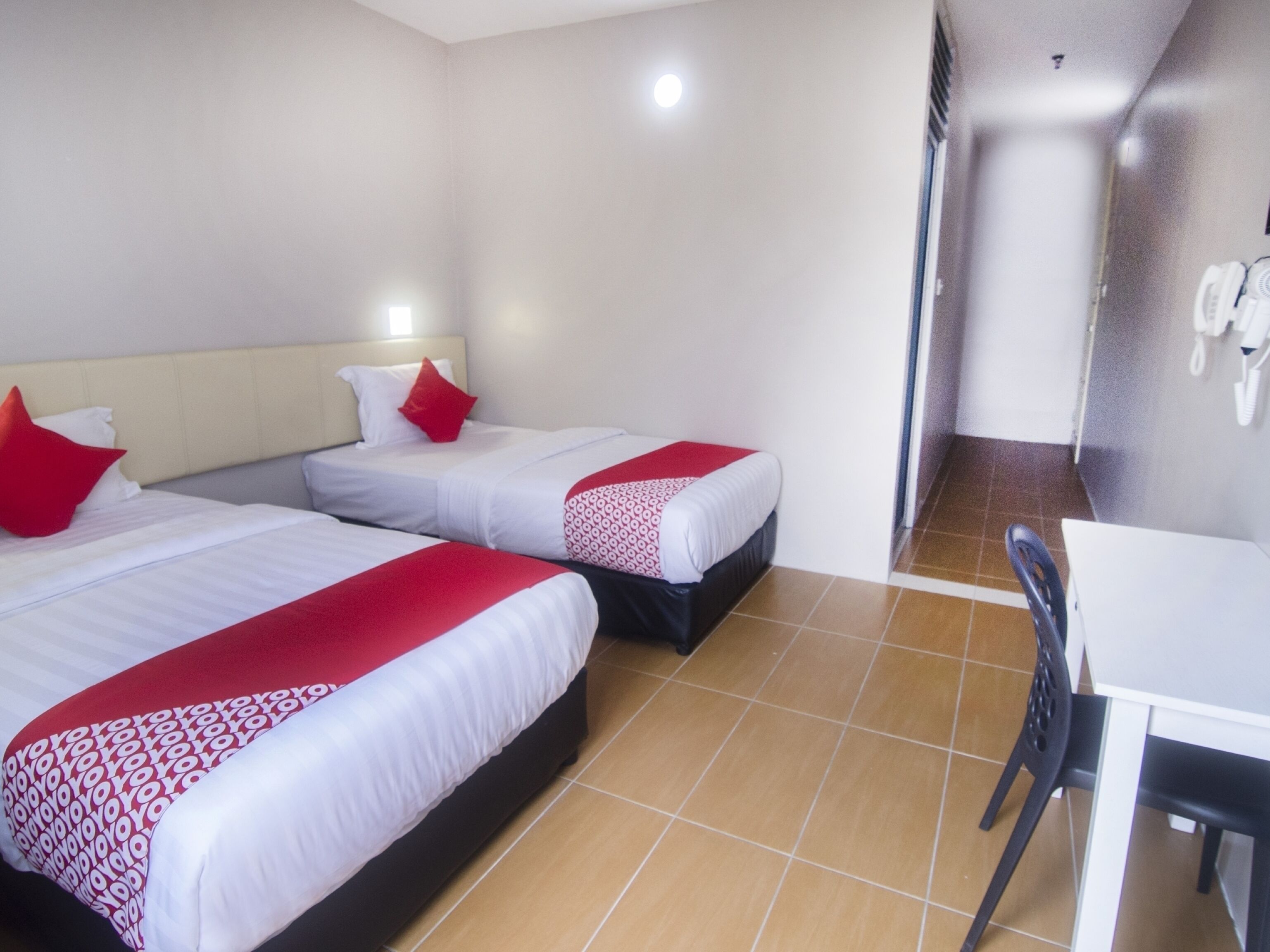 Habitación de hotel con dos camas, cada una con ropa de cama roja y blanca, un escritorio blanco y una silla.
