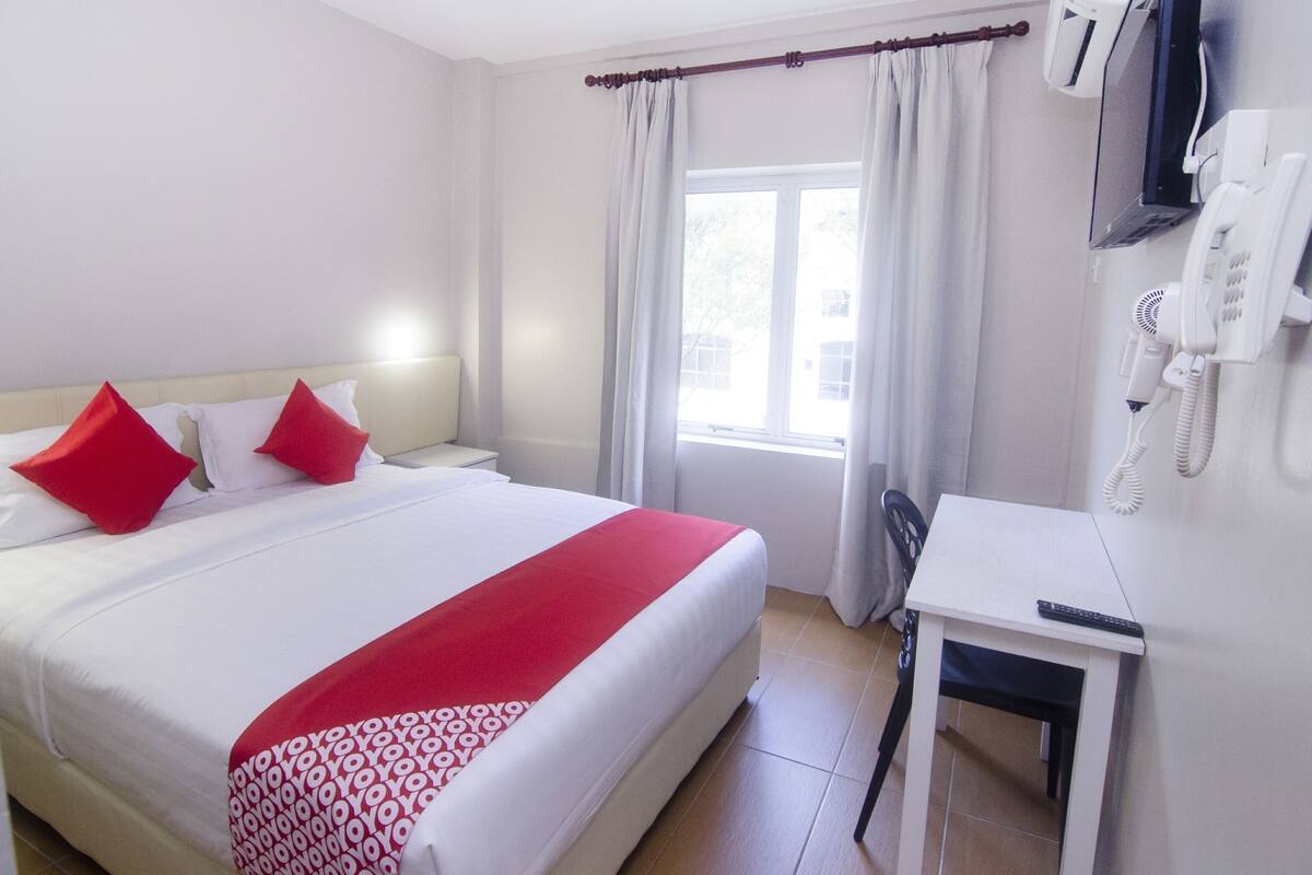 Une chambre d’hôtel avec un lit, un bureau, un téléphone et une fenêtre avec des rideaux.