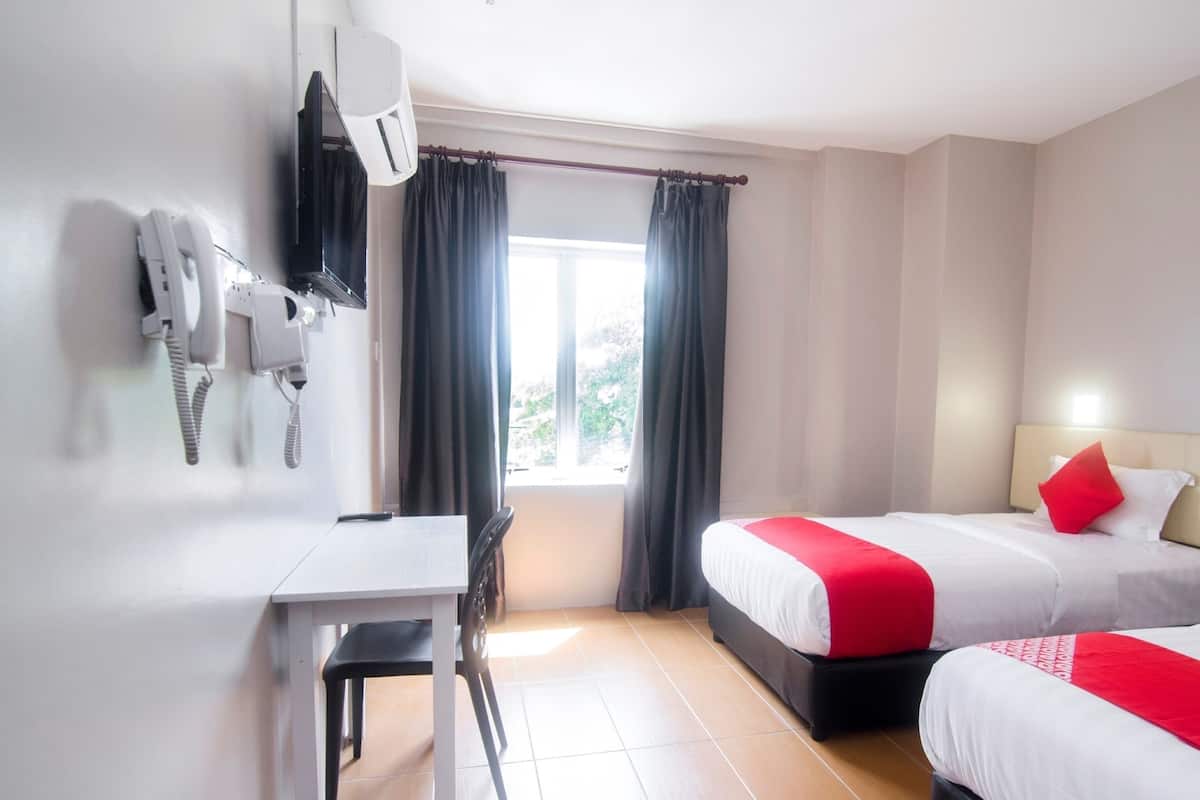 Une chambre d’hôtel équipée d’un bureau, de deux lits, d’un téléphone et d’une fenêtre avec des rideaux.