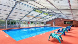 An indoor swimming pool with clear glass ceilings, a brick wall, and blue pool chairs.