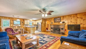 A cozy cabin interior with a wooden interior, a fireplace, a ceiling fan, and a television.