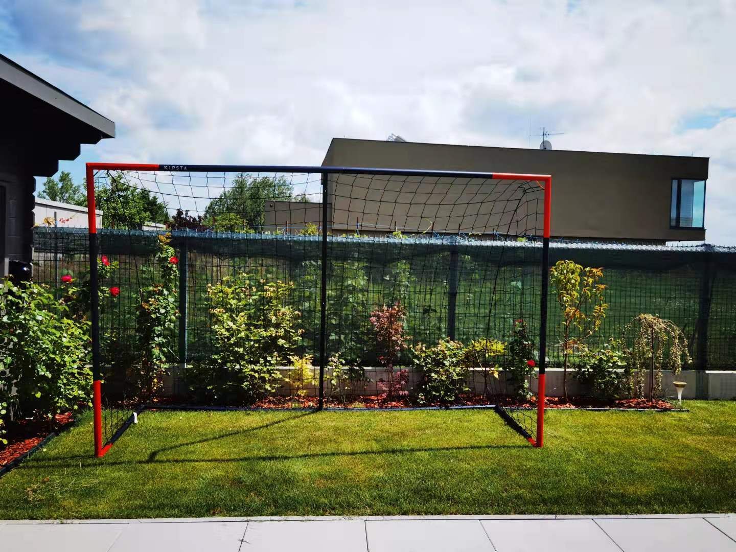 Un but de football installé dans un jardin, avec une maison en arrière-plan.