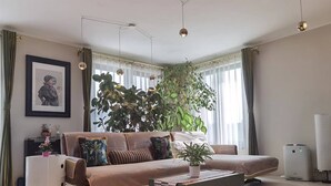 Ett modernt vardagsrum med en soffa, ett soffbord, en stor växt och en inramad tavla på väggen.
