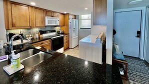 Una cocina moderna con encimeras de granito, armarios de madera, microondas integrado y refrigerador.