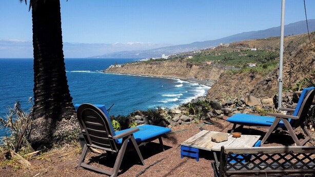A coastal view with a wooden table and two blue chairs overlooking the ocean. - Home2Book Atlantic View Rustic Villa (Los Realejos)