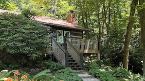 A wooden cabin with a stone chimney, surrounded by lush greenery and a gravel pathway leading to a wooden deck. - PEACOCK RIDGE Great location, minutes from Blowing Rock and Appalachian Ski Mtn! (Blowing Rock)