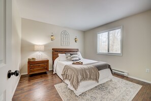 Une chambre à coucher avec une tête de lit en bois, une table de chevet avec une lampe, un grand lit recouvert d’un tapis à motifs et une fenêtre avec des stores.