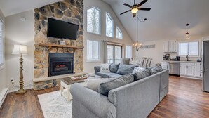A spacious living room with a stone fireplace, a large gray sectional sofa, and a television mounted on the wall. - Poconos Hideaway Hot Tub, Zen Garden & Fire Pit, hiking and water parks nearby. (Albrightsville)