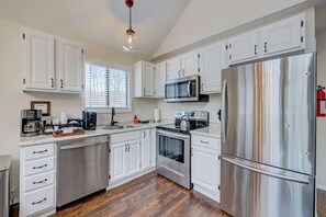 Une cuisine moderne avec des armoires blanches, des appareils en acier inoxydable et un plancher en bois.