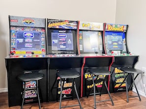 Vier speelautomaten met krukken ervoor, voorzien van verschillende spellen zoals 'Asteroids' en 'Pac-Man'.