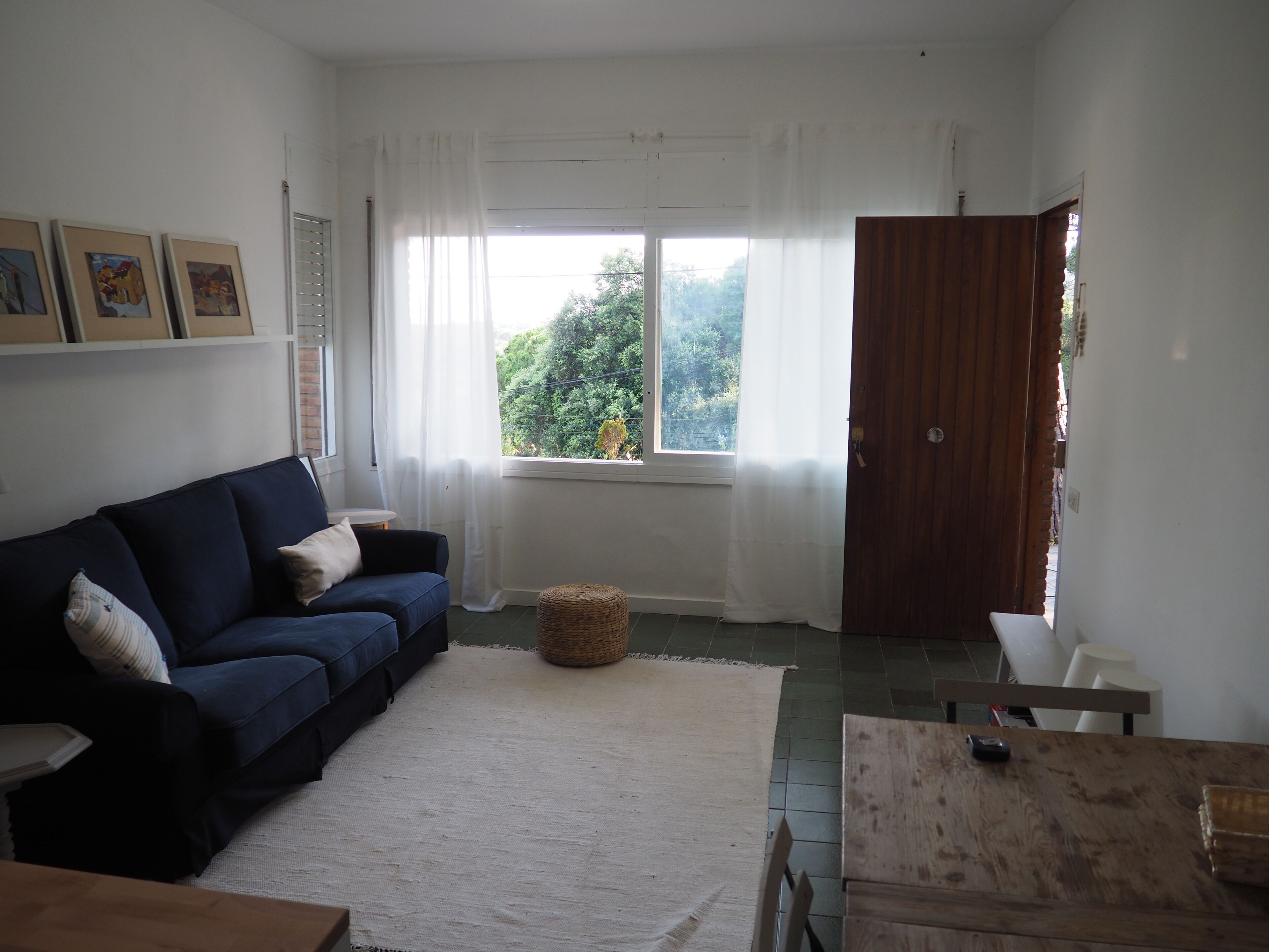 A living room with a dark blue sofa, a white rug, a wooden table, and a window with sheer curtains.