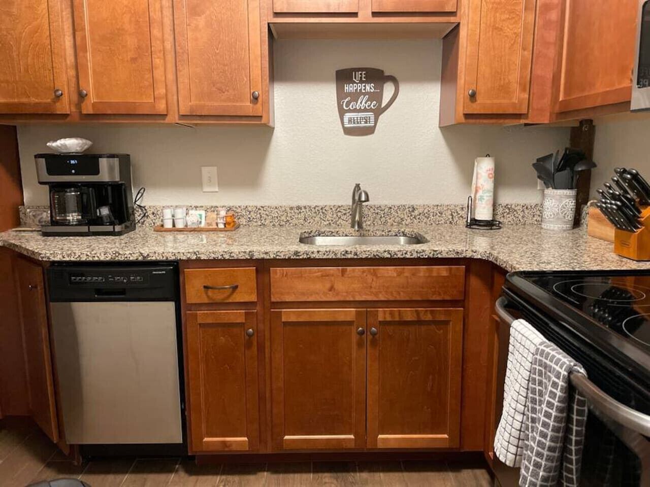 A kitchen with wooden cabinets, a granite countertop, a coffee maker, a dishwasher, and a stove.
