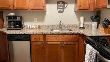 A kitchen with wooden cabinets, a granite countertop, a coffee maker, a dishwasher, and a stove.
