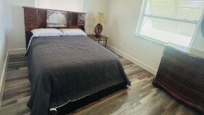 A bedroom with a bed, a nightstand, a lamp, a dresser, a ceiling fan, and a window with blinds. - Two bedrooms cute and cozy house in Melbourne (Melbourne)