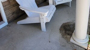 Een veranda met twee witte Adirondack-stoelen, een raam met zwarte luiken en een lamp.