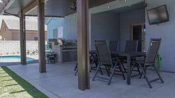 An outdoor patio with a grill, dining table, and chairs.