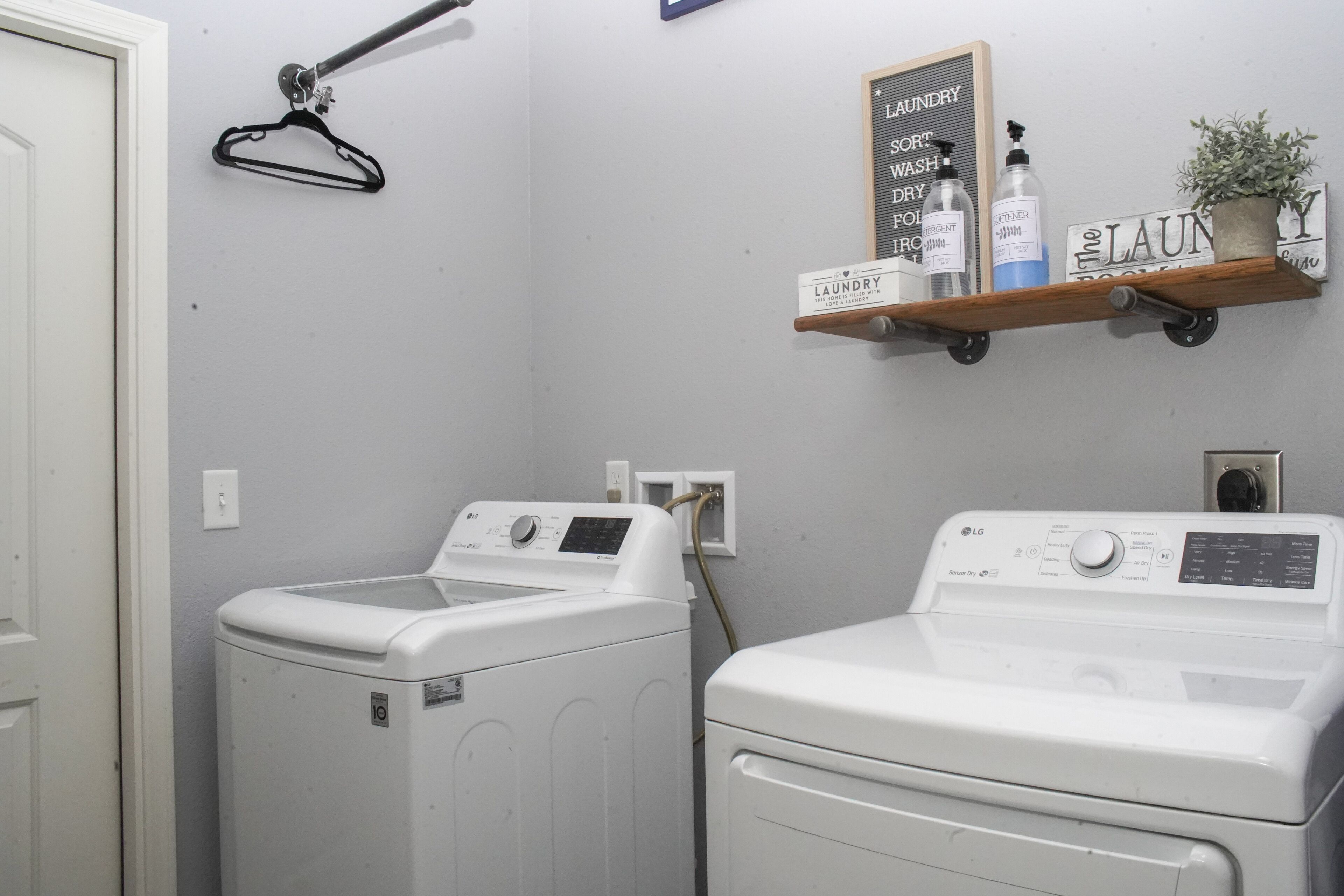 A laundry area with two white front-loading washers and dryers, a wall-mounted shelf with laundry supplies, and a hanging rack.
