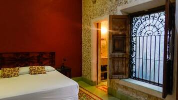 Un dormitorio con cama, cabecera de madera, ventana con rejas y pared roja.