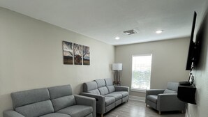 A spacious living room with grey sofas, a flat-screen TV mounted on the wall, and a floor lamp. - Adorable 2 bedroom guest house! Minutes from downtown (Houston)